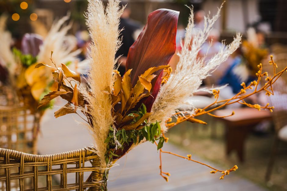 A floral arrangement featuring a variety of dried and preserved flowers mounted on a wicker chair, suitable for floral gifts or wedding decor. The bouquet includes tall, fluffy pampas grass in cream t